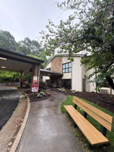 A freshly washed commercial building entrance with clean siding, stone façade, and walkways leading past landscaped flower beds and a bench